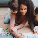 Mother sitting with two children calmly coloring together in a cozy home setting, showing connection and co-regulation.