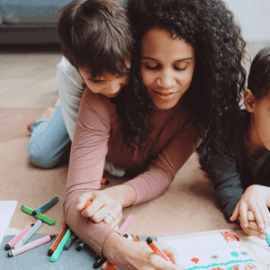 Mother sitting with two children calmly coloring together in a cozy home setting, showing connection and co-regulation.