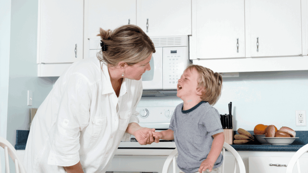 Calm mother sitting with crying child showing emotional regulation and parental leadership during a meltdown