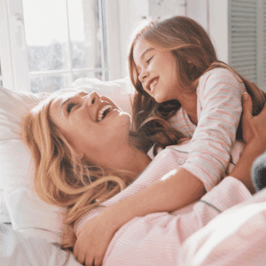 A happy mother and daughter laughing together on a bed, illustrating how to break the cycle of reactive parenting.