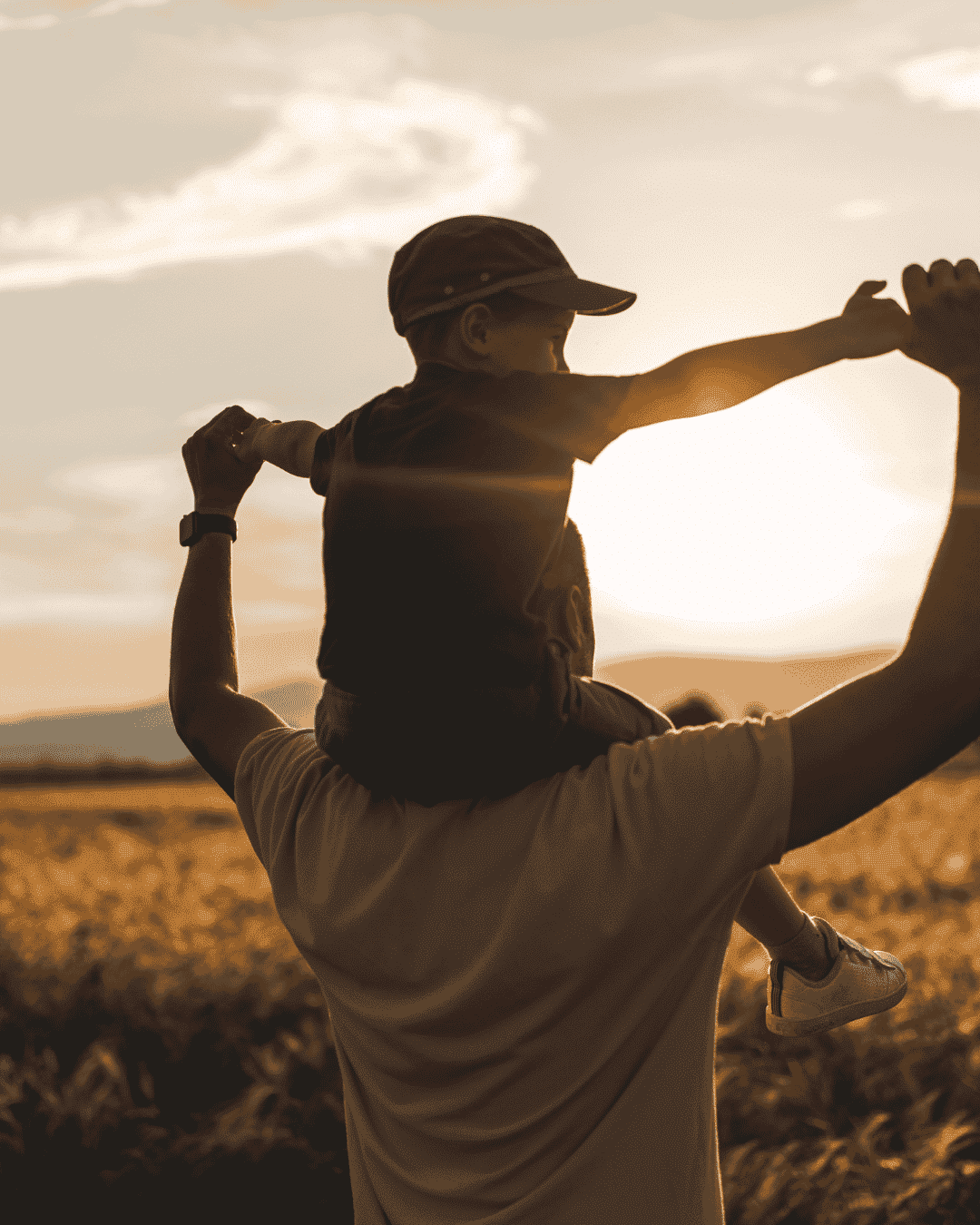 Un père portant son fils sur ses épaules dans un champ au coucher du soleil, illustrant la liberté et la vitalité retrouvées grâce au coaching parental.